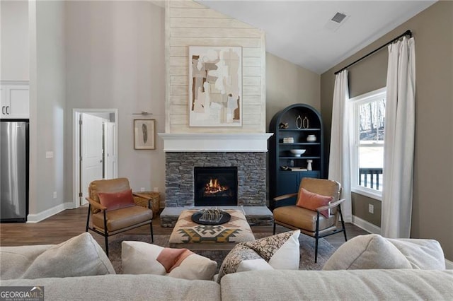 living area featuring visible vents, dark wood-type flooring, a stone fireplace, high vaulted ceiling, and baseboards