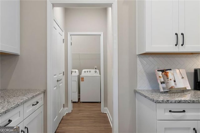 kitchen featuring light wood finished floors, light stone counters, washing machine and dryer, and white cabinetry