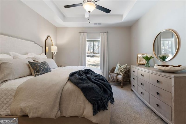 bedroom with light carpet, visible vents, a tray ceiling, and ceiling fan