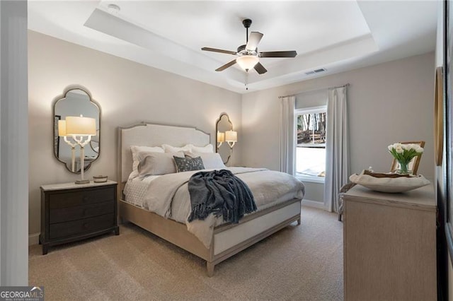 bedroom featuring a tray ceiling, light carpet, visible vents, and baseboards