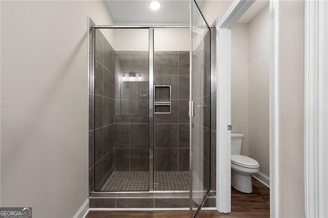 full bathroom featuring a stall shower, baseboards, toilet, and wood finished floors