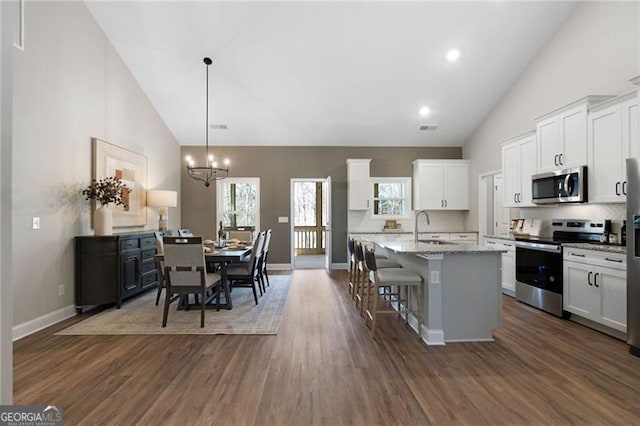 kitchen featuring light stone counters, stainless steel appliances, a kitchen island with sink, a sink, and white cabinetry