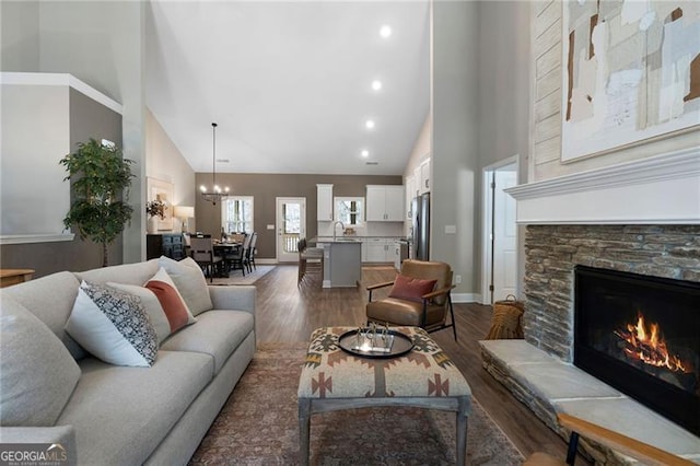 living room featuring dark wood-style floors, baseboards, high vaulted ceiling, and a stone fireplace