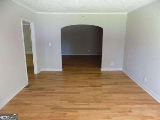 spare room featuring crown molding, light hardwood / wood-style floors, and a textured ceiling