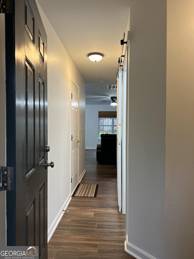 hallway featuring dark wood-type flooring and a barn door