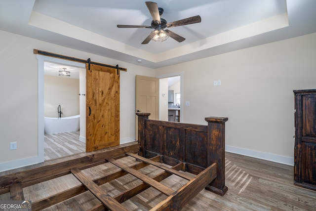 bedroom featuring dark wood-type flooring, a raised ceiling, ceiling fan, and a barn door