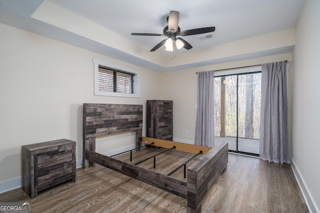 bedroom with hardwood / wood-style flooring, access to outside, a raised ceiling, and ceiling fan