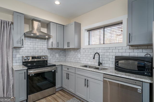 kitchen featuring wall chimney range hood, sink, gray cabinets, appliances with stainless steel finishes, and light stone countertops