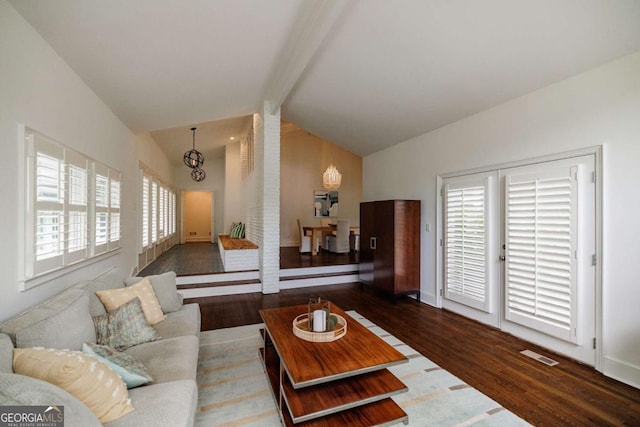 living room featuring lofted ceiling with beams, dark wood-type flooring, and a chandelier