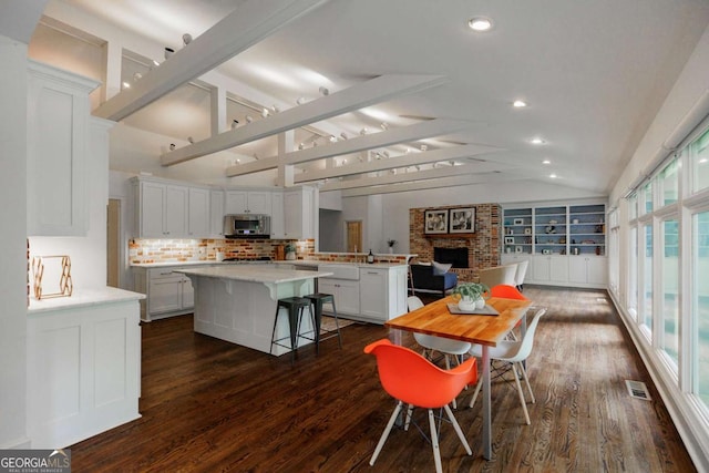 dining room with a fireplace, dark hardwood / wood-style floors, and vaulted ceiling with beams