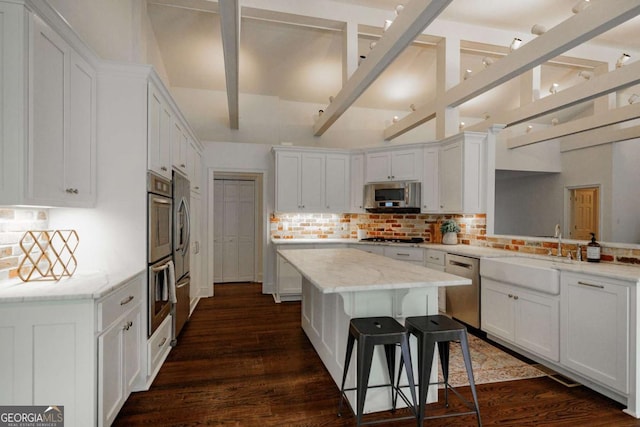 kitchen featuring appliances with stainless steel finishes, white cabinetry, a center island, light stone counters, and a kitchen bar