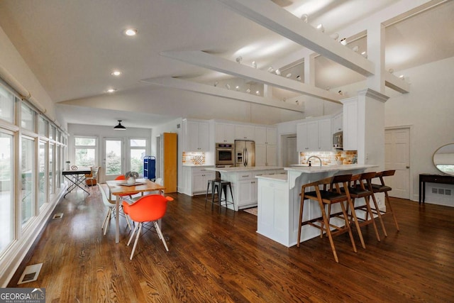 kitchen with dark wood-type flooring, a breakfast bar, appliances with stainless steel finishes, white cabinets, and decorative backsplash