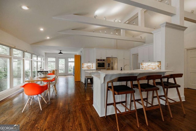 kitchen with white cabinetry, backsplash, stainless steel appliances, and a kitchen bar