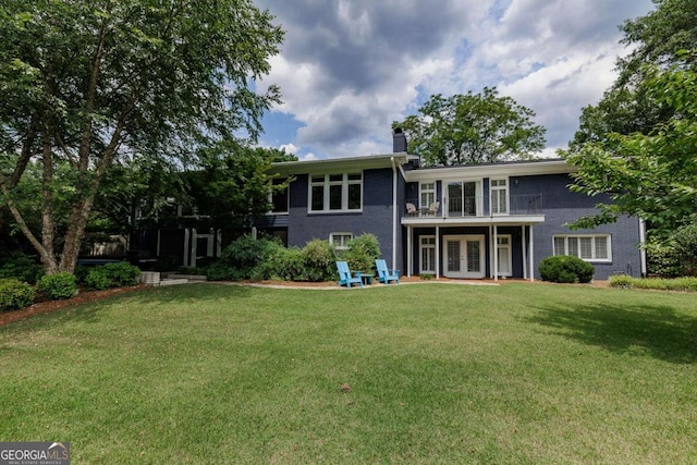 rear view of property featuring a yard, french doors, and a balcony