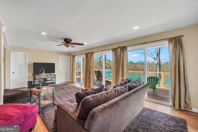 living room with a water view, ceiling fan, and light wood-type flooring