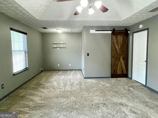 empty room with ceiling fan, a barn door, a textured ceiling, and carpet