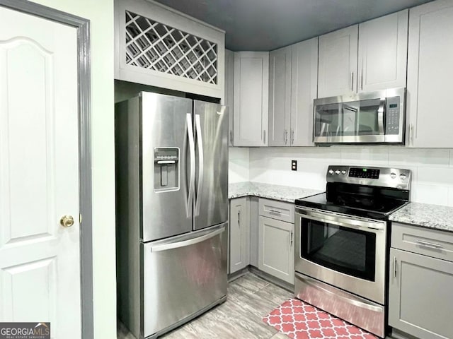 kitchen with stainless steel appliances, light stone countertops, and gray cabinetry