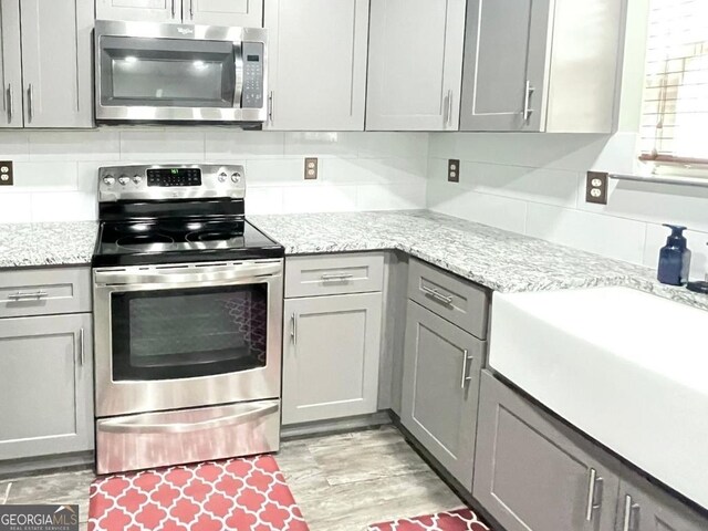 kitchen with light stone counters, gray cabinets, and stainless steel appliances