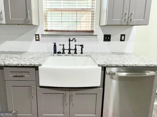 kitchen with sink, gray cabinetry, stainless steel dishwasher, light stone countertops, and decorative backsplash