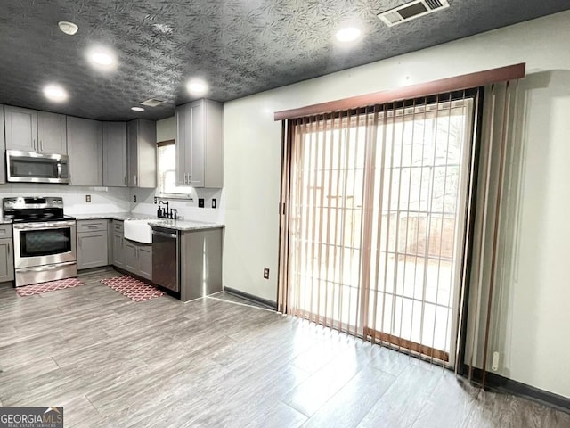 kitchen with appliances with stainless steel finishes, light hardwood / wood-style flooring, a textured ceiling, gray cabinets, and sink