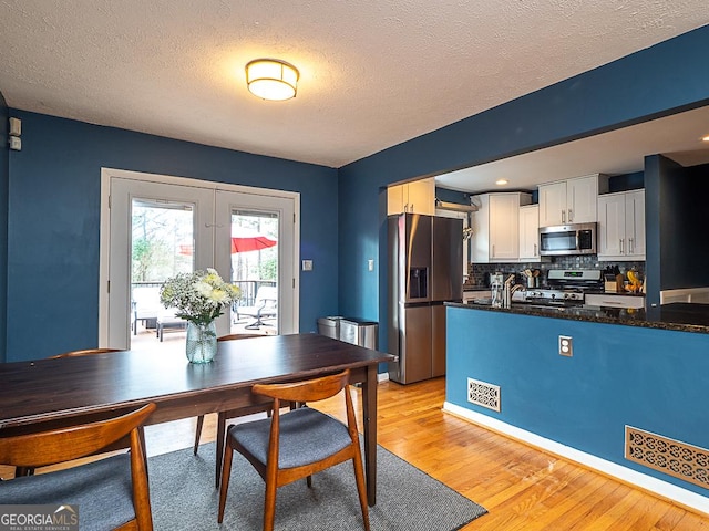 kitchen featuring french doors, white cabinetry, tasteful backsplash, light hardwood / wood-style flooring, and appliances with stainless steel finishes