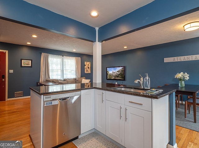 kitchen with sink, dark stone countertops, white cabinets, stainless steel dishwasher, and kitchen peninsula