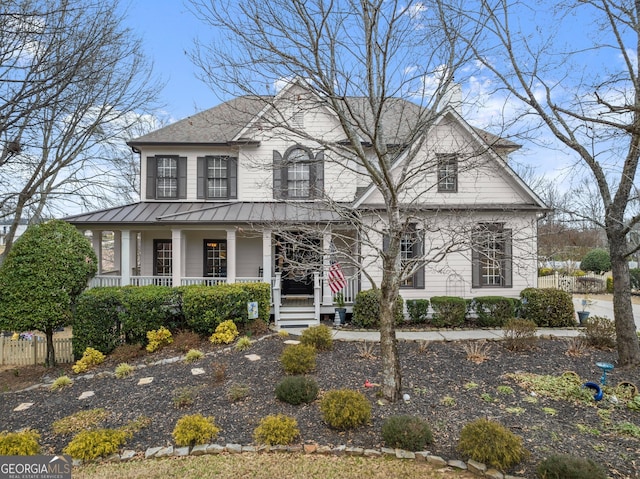 view of front facade featuring covered porch, metal roof, a standing seam roof, and fence