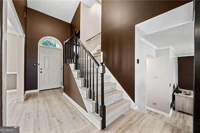 entryway featuring crown molding, a textured ceiling, and light wood-type flooring