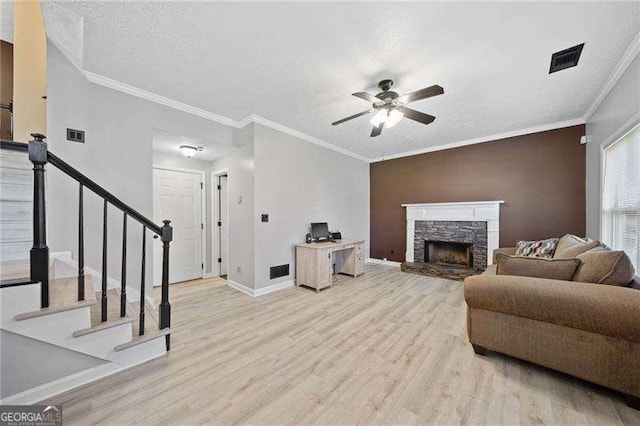 living room with a stone fireplace, light hardwood / wood-style flooring, a textured ceiling, ornamental molding, and ceiling fan