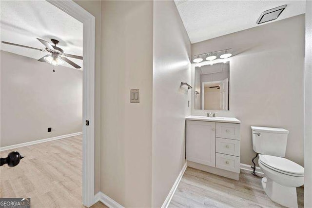 bathroom featuring wood-type flooring, vanity, ceiling fan, toilet, and a textured ceiling