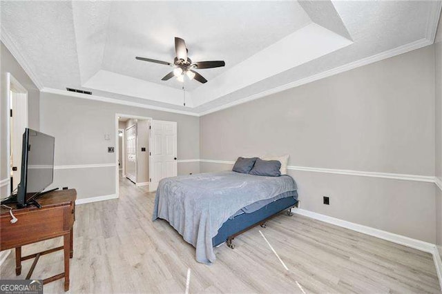 bedroom with a tray ceiling, ornamental molding, light hardwood / wood-style floors, and ceiling fan