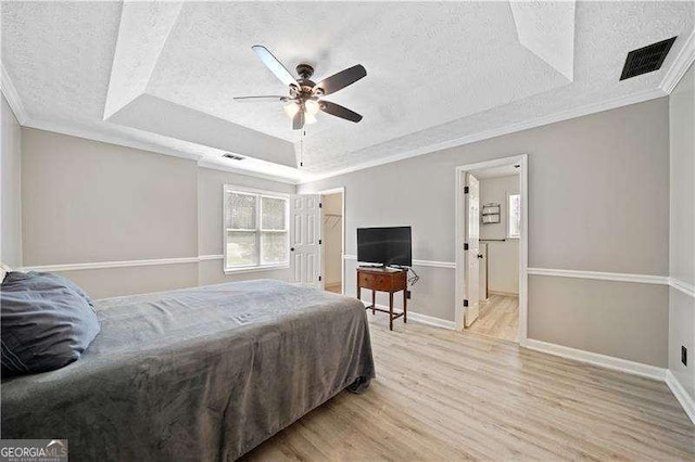 bedroom featuring ornamental molding, light hardwood / wood-style floors, a raised ceiling, and a textured ceiling