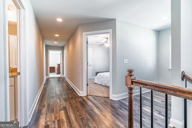 hall featuring dark wood-style floors, recessed lighting, baseboards, and an upstairs landing