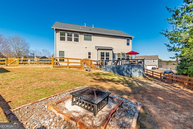 back of property with a fire pit, a yard, a fenced backyard, and a wooden deck