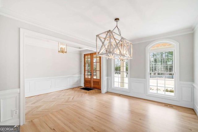 unfurnished dining area featuring an inviting chandelier, crown molding, and light parquet flooring