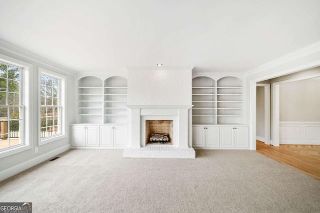 unfurnished living room with ornamental molding, a brick fireplace, light carpet, and built in shelves