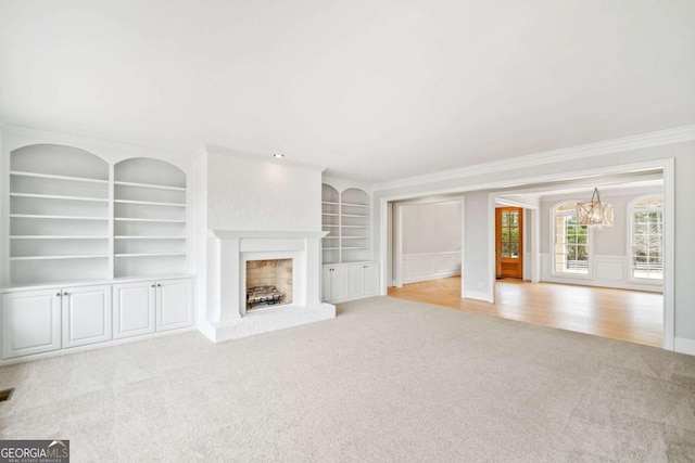 unfurnished living room with an inviting chandelier, a brick fireplace, light carpet, and ornamental molding