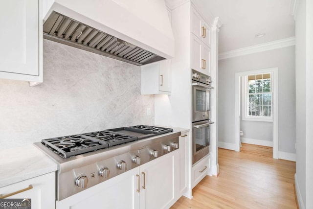 kitchen featuring white cabinetry, crown molding, wall chimney exhaust hood, and appliances with stainless steel finishes