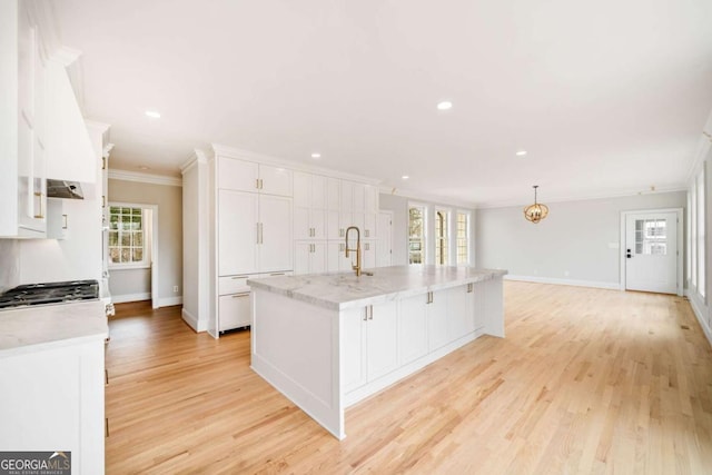 kitchen featuring ornamental molding, a wealth of natural light, a kitchen island with sink, and white cabinets