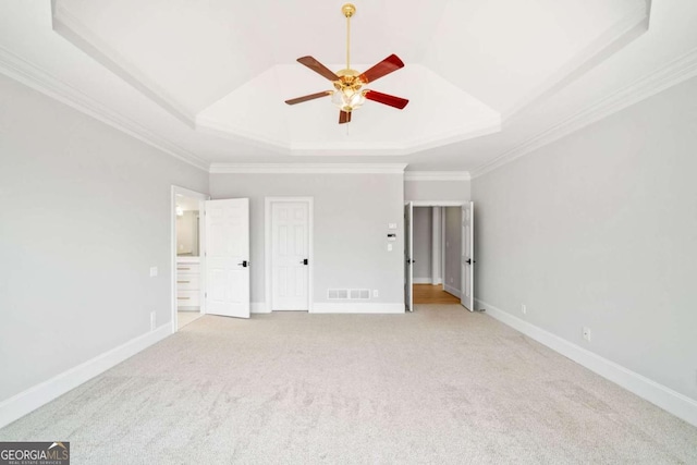 unfurnished bedroom featuring ceiling fan, ensuite bathroom, ornamental molding, light carpet, and a raised ceiling