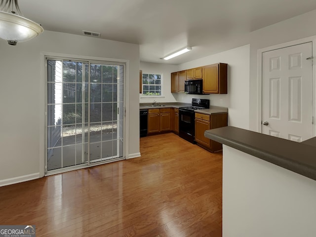 kitchen with decorative light fixtures, light hardwood / wood-style floors, sink, and black appliances