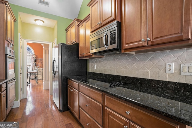 kitchen featuring dark stone countertops, tasteful backsplash, stainless steel appliances, and light hardwood / wood-style flooring