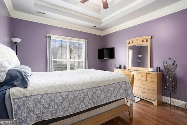 bedroom featuring a tray ceiling, dark wood-type flooring, ornamental molding, and ceiling fan