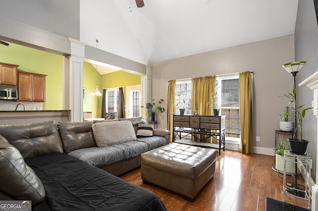 living room featuring dark wood-type flooring, ceiling fan, high vaulted ceiling, and decorative columns