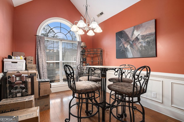 dining room with hardwood / wood-style flooring, bar area, high vaulted ceiling, and a notable chandelier