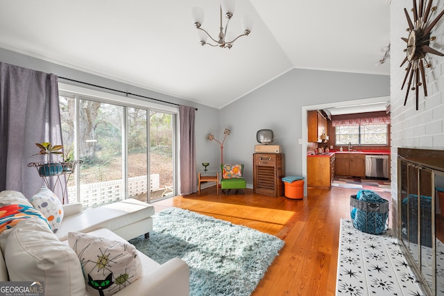 living room featuring lofted ceiling, sink, wood-type flooring, a notable chandelier, and a fireplace