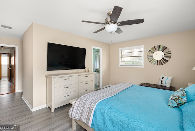 bedroom featuring multiple windows, ceiling fan, connected bathroom, and light wood-type flooring