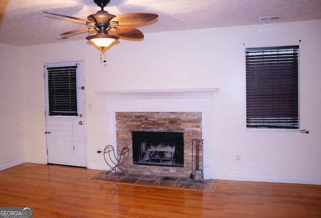 unfurnished living room featuring ceiling fan, wood-type flooring, a fireplace, and a textured ceiling