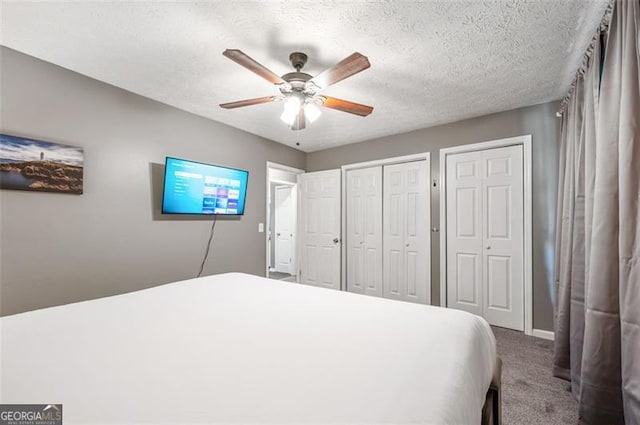 carpeted bedroom with ceiling fan, two closets, and a textured ceiling