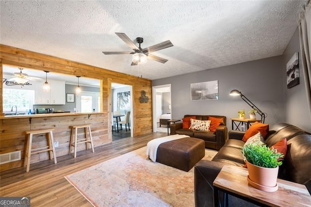 living room with a textured ceiling, wood walls, ceiling fan, and light hardwood / wood-style flooring